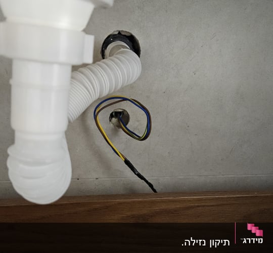 צינור פלסטיק לבן מתחת לכיור עם חוטי חשמל